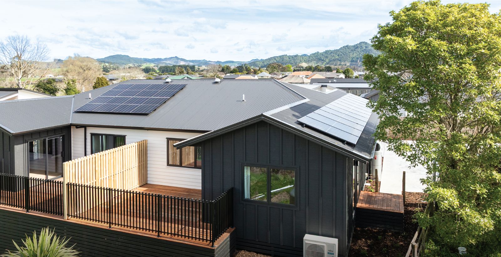 A finished new home with a deck, looking out to green hills