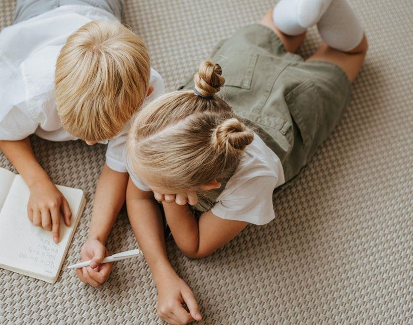 Two children drawing on a soft carpet